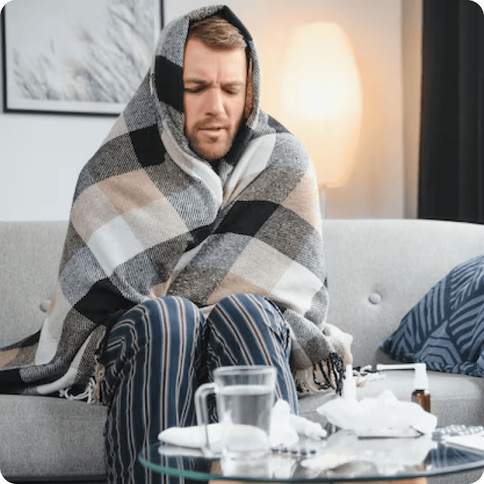 Людина в кімнаті, зодягнена в плед від холоду біля вікна