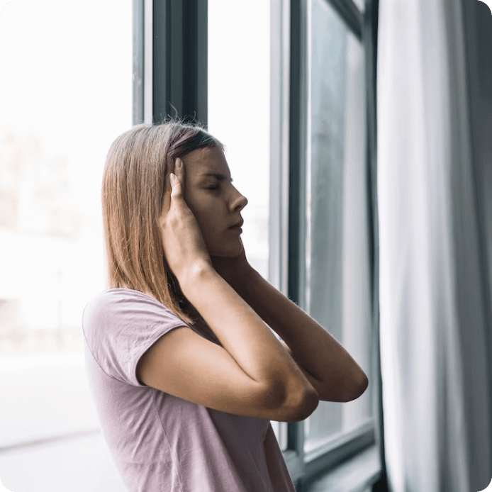 Жінка біля вікна закриває вуха від шуму